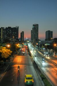 An urban street scene at dusk with towering buildings and moving traffic under the city lights.